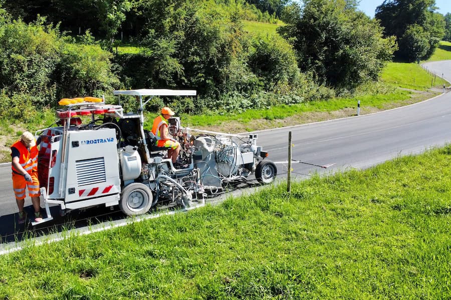 Einige Mitarbeiter in Warnwesten markieren einen Fahrbahnrand auf einer ruhigen Landstraße